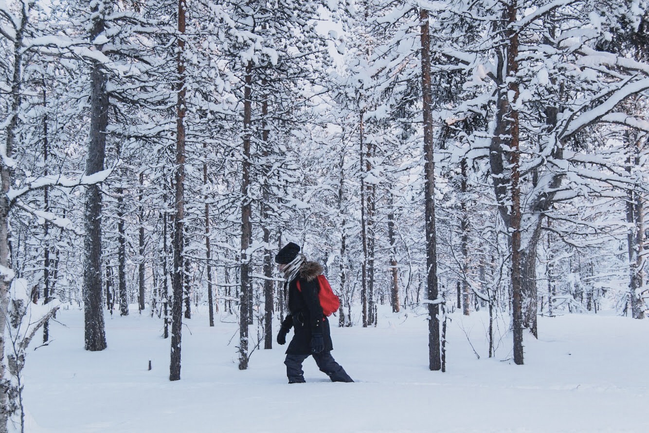 Mulher caminha na neve profunda em floresta na Finlândia