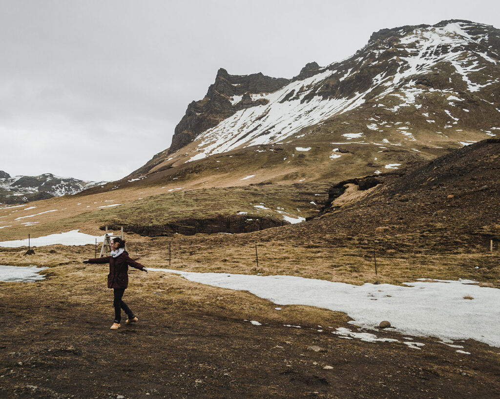 Mulher no meio do campo com montanhas e neve na Islândia