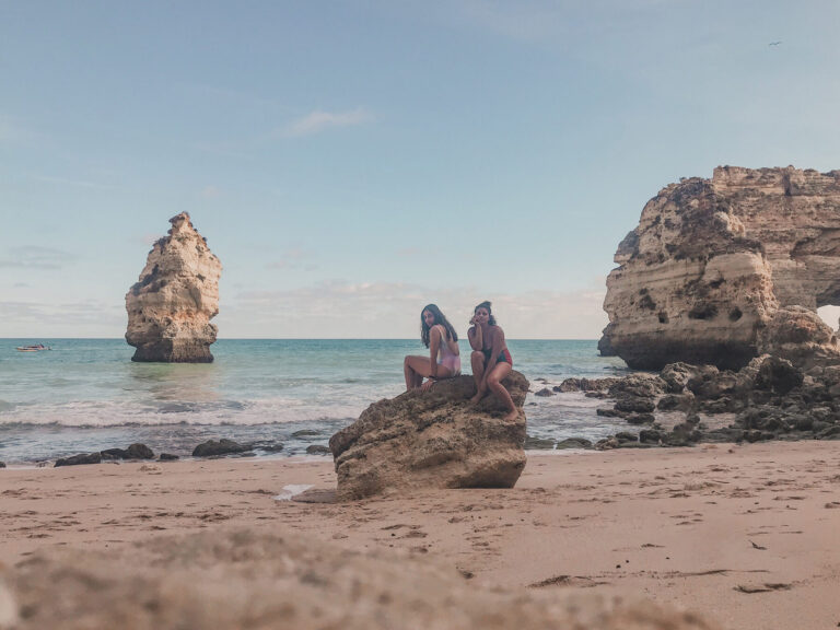 duas mulheres amigas sentadas na pedra da praia da marinha de costas para o mar no algarve em portugal