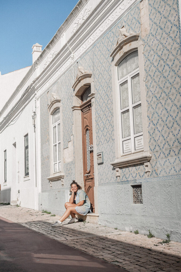 mulher sentada em frente a porta de uma casa de ladrinhos portugueses azuis em albufeira portugal