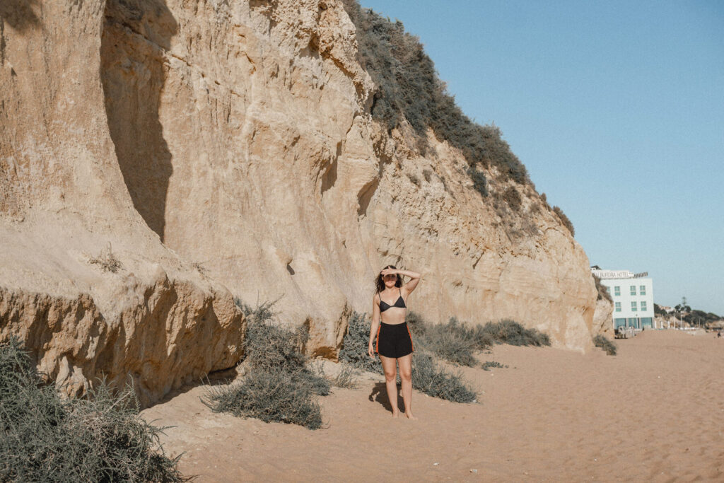 mulher tapa o rosto do sol na praia vestindo short preto na praia do peneco em albufeira portugal