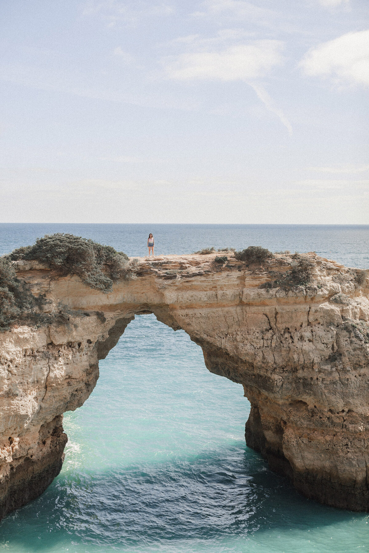 mulher em pé sobre o arco de albandeira com agua azul do mar abaixo no algarve em portugal