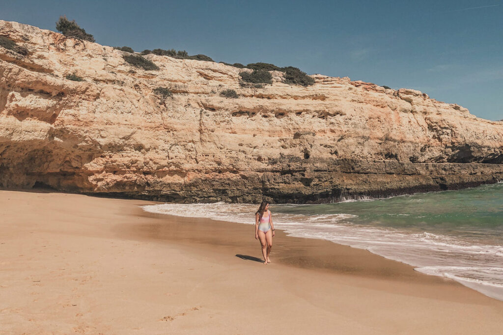 mulher na praia de albandeira anda de maiô observando as ondas do mar do algarve em portugal